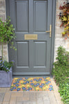 RHS Bloom Collection coir doormat with blue spring flowers in front of a grey door