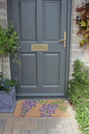 Atlantic Mats RHS Bloom Collection coir doormat with purple wisteria design in front of a grey door