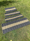 Four sizes of Atlantic Mats grey and tan striped recycled rope doormats on green grass.