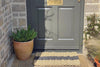 Atlantic Mats Grey Stripe Rope Outdoor Doormat in front of a grey door with a potted plant.