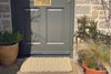 Natural coloured Atlantic Mats outdoor rope doormat in front of a grey door and stone wall.