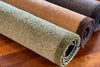 Three rolled recycled washable doormats in natural colors on a wooden surface